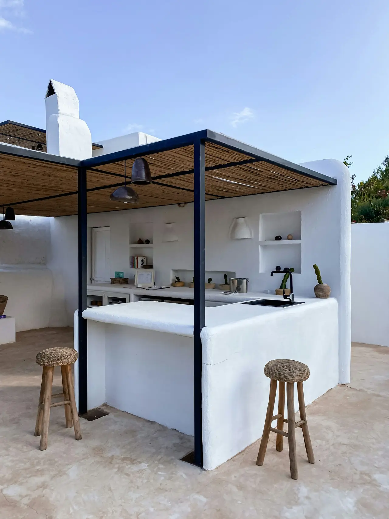 Bar externo com balcão branco, banquetas de madeira e pergolado