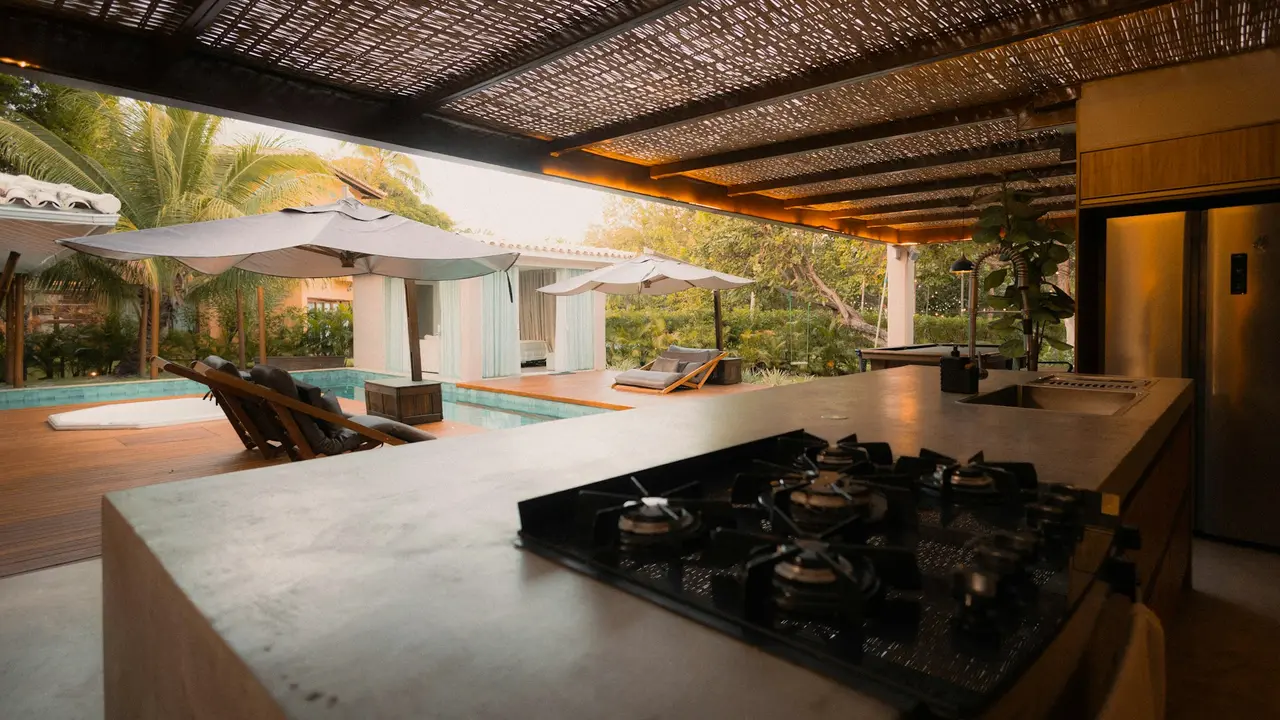 Cozinha externa com cooktop embutido em bancada de pedra ao lado da piscina
