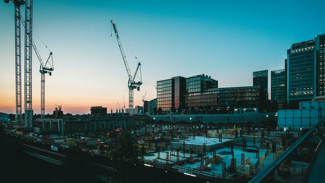 Guindastes de obra ao entardecer, com prédios ao fundo